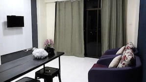 A living room with a black table, a purple sofa, a TV mounted on the wall, and a sliding glass door with curtains. - SUNSET View Studio Apartment (Langkawi)
