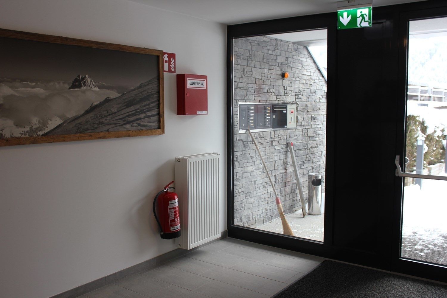 A room with a fire extinguisher, a radiator, a painting, and a view of the outside.