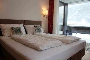 Una cama doble con dos almohadones decorativos, una lámpara de pared y vistas a un paisaje nevado a través de un ventanal grande.