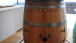 Um barril de madeira transformado em mesa, com dois copos de vinho e garrafas em cima.