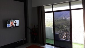 Una habitación con televisión en la pared, ventilador de techo y un amplio ventanal con vistas a un paisaje montañoso.