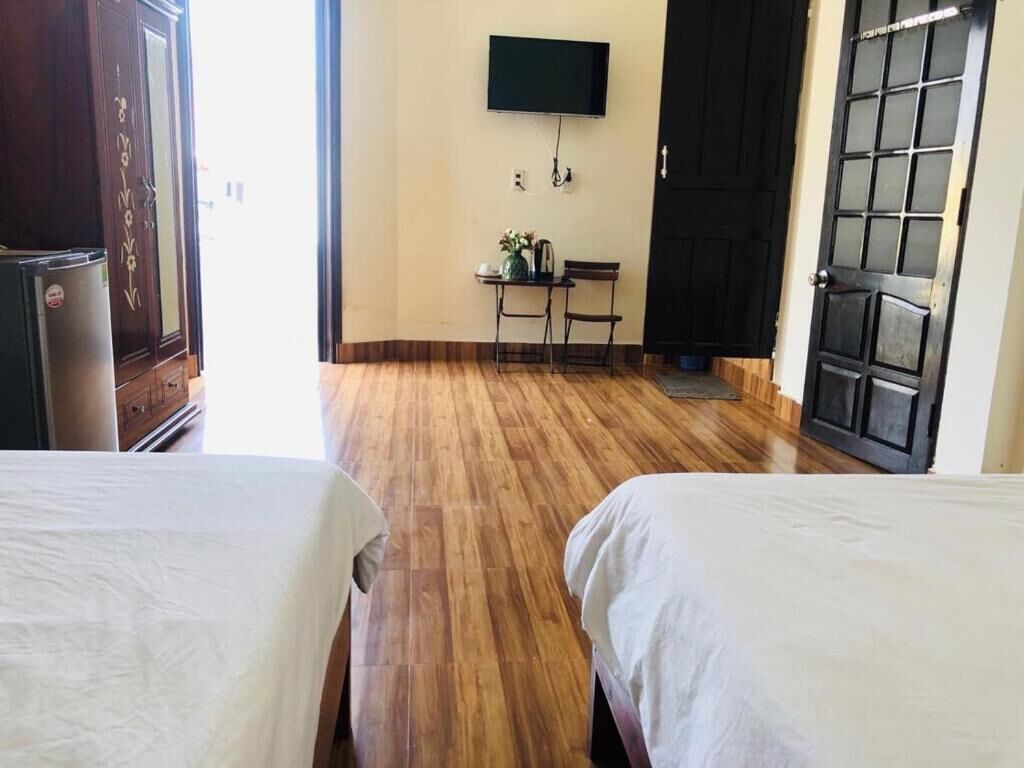 Een hotelkamer met twee bedden, een aan de muur bevestigde televisie, een klein tafeltje met een vaas en een deur met een geëtste glazen ruit.