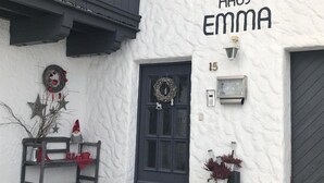 Un bâtiment à l’extérieur blanc et à la porte noire. Le nom « HAUS EMMA » est inscrit au-dessus de la porte. On peut voir le numéro « 15 » sur le mur, à droite de la porte.