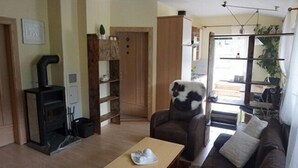 Un salon avec une cheminée, un canapé, une table basse et un fauteuil recouvert d’un plaid en fourrure.