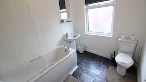 Een badkamer met een bad, wastafel, toilet en een raam voor natuurlijk licht.