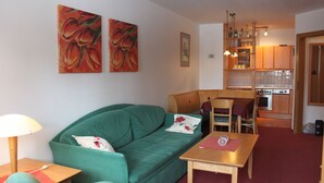 Una sala de estar con un sofá verde, una mesa de madera y una cocina al fondo.