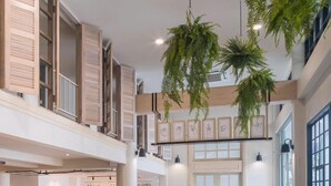 A spacious, modern interior with a high ceiling, wooden shutters, and hanging plants. - The Blanket Hotel (Phuket)