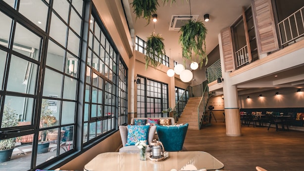 A spacious indoor area with large windows, hanging plants, and a staircase. - The Blanket Hotel (Phuket)