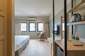 A hotel room with a bed, a chair, a table, and a shelf with bottles and a kettle. - The Blanket Hotel Phuket Old town (Phuket)