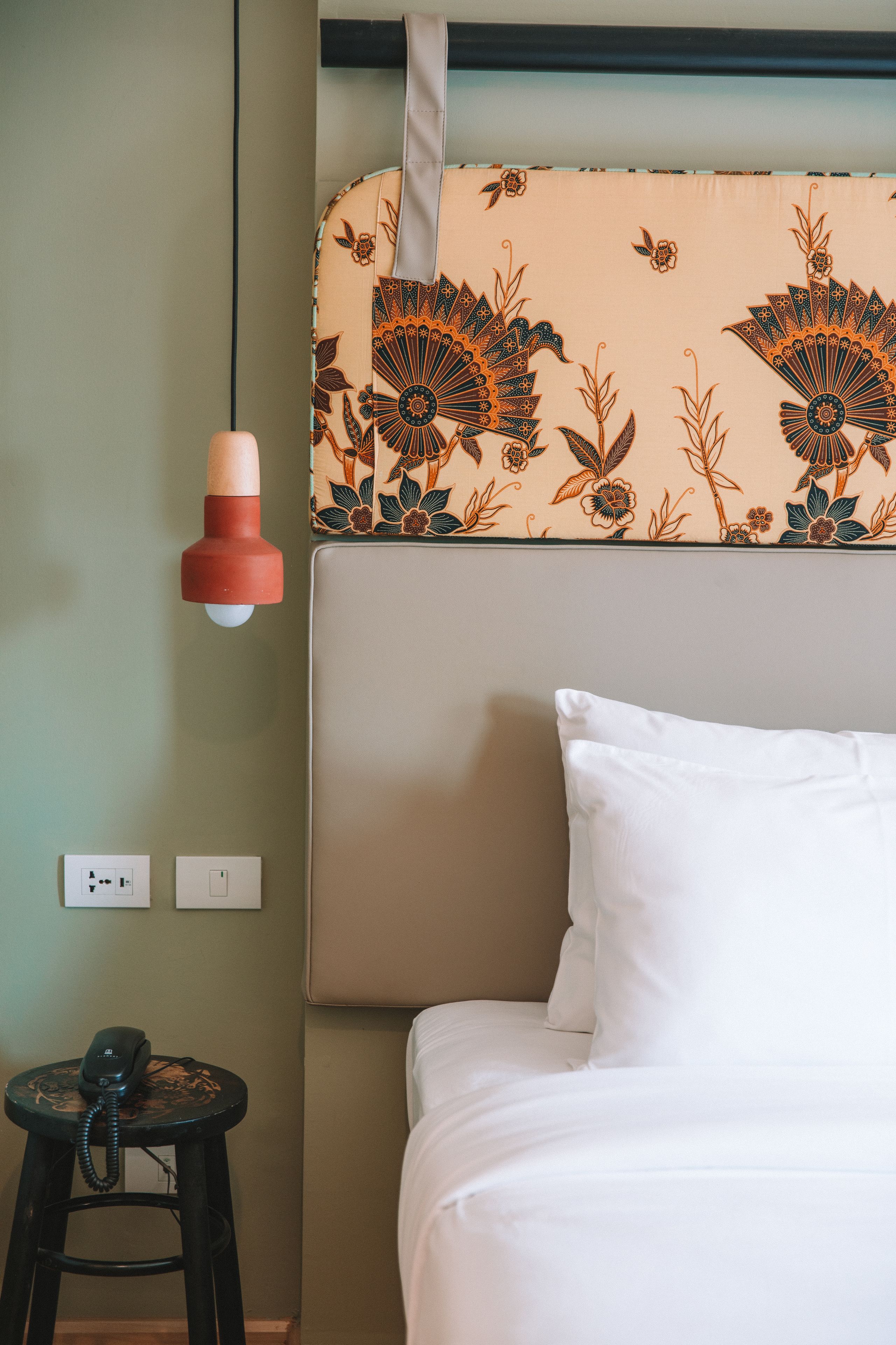A hotel room with a bed, a wall-mounted telephone, and a decorative headboard.
