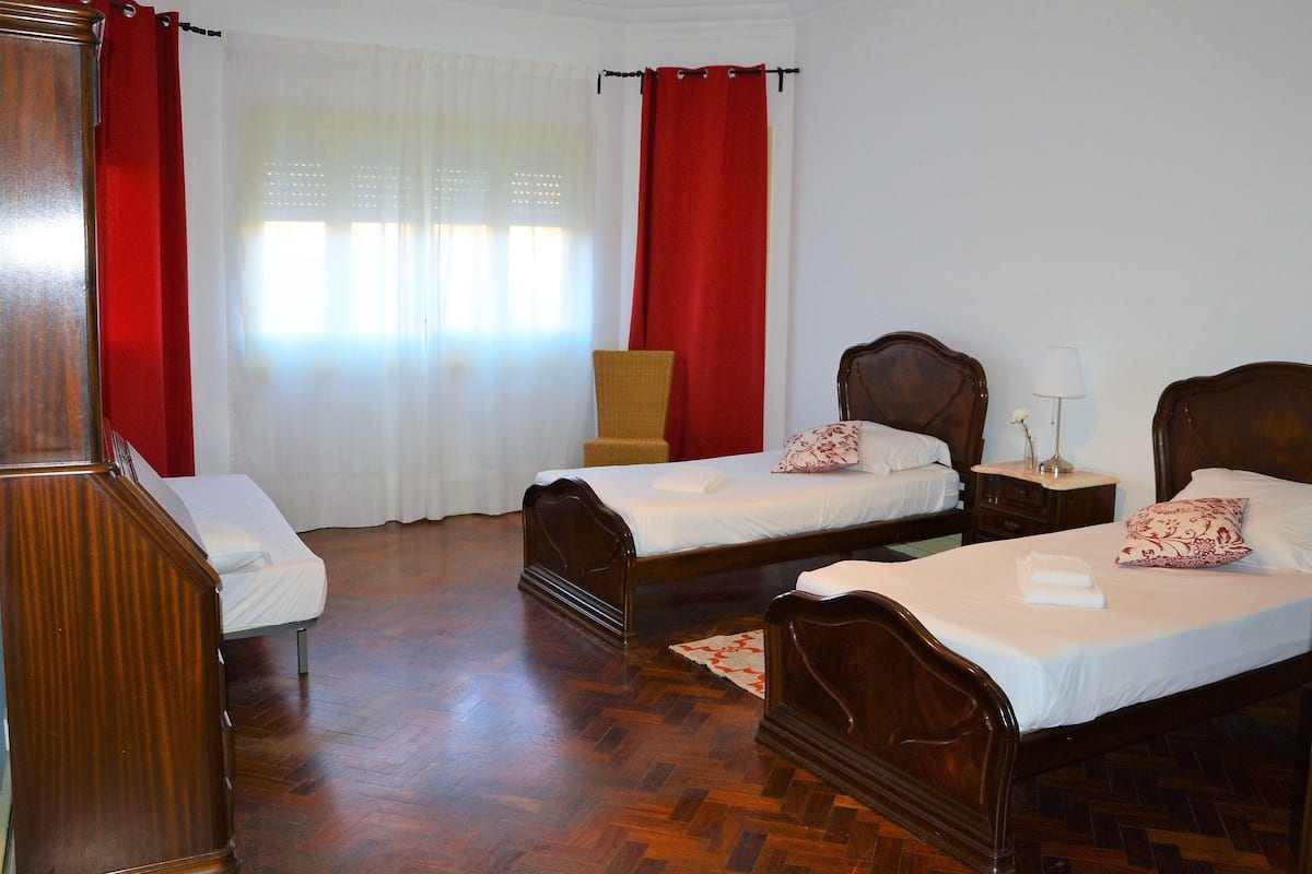A room with two wooden beds, a wooden wardrobe, a chair, and a window with curtains.