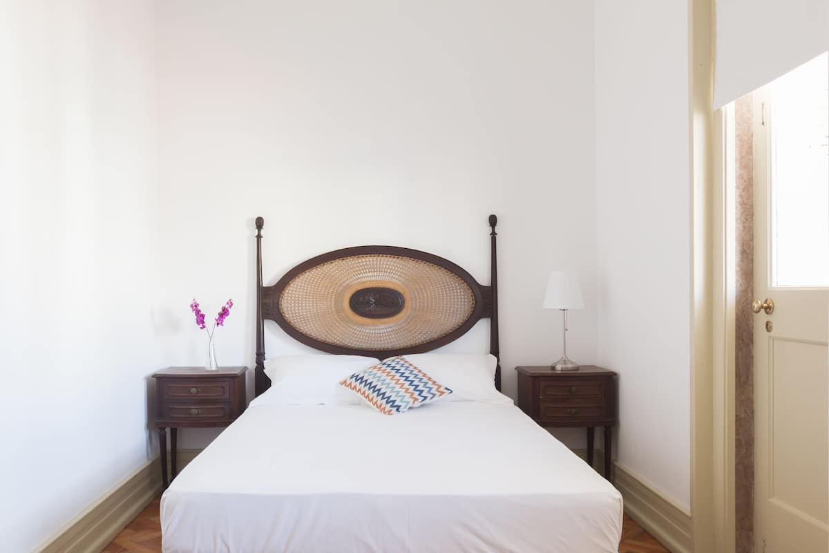 A neatly made bed with a woven headboard, two bedside tables with lamps, and a door to the right.