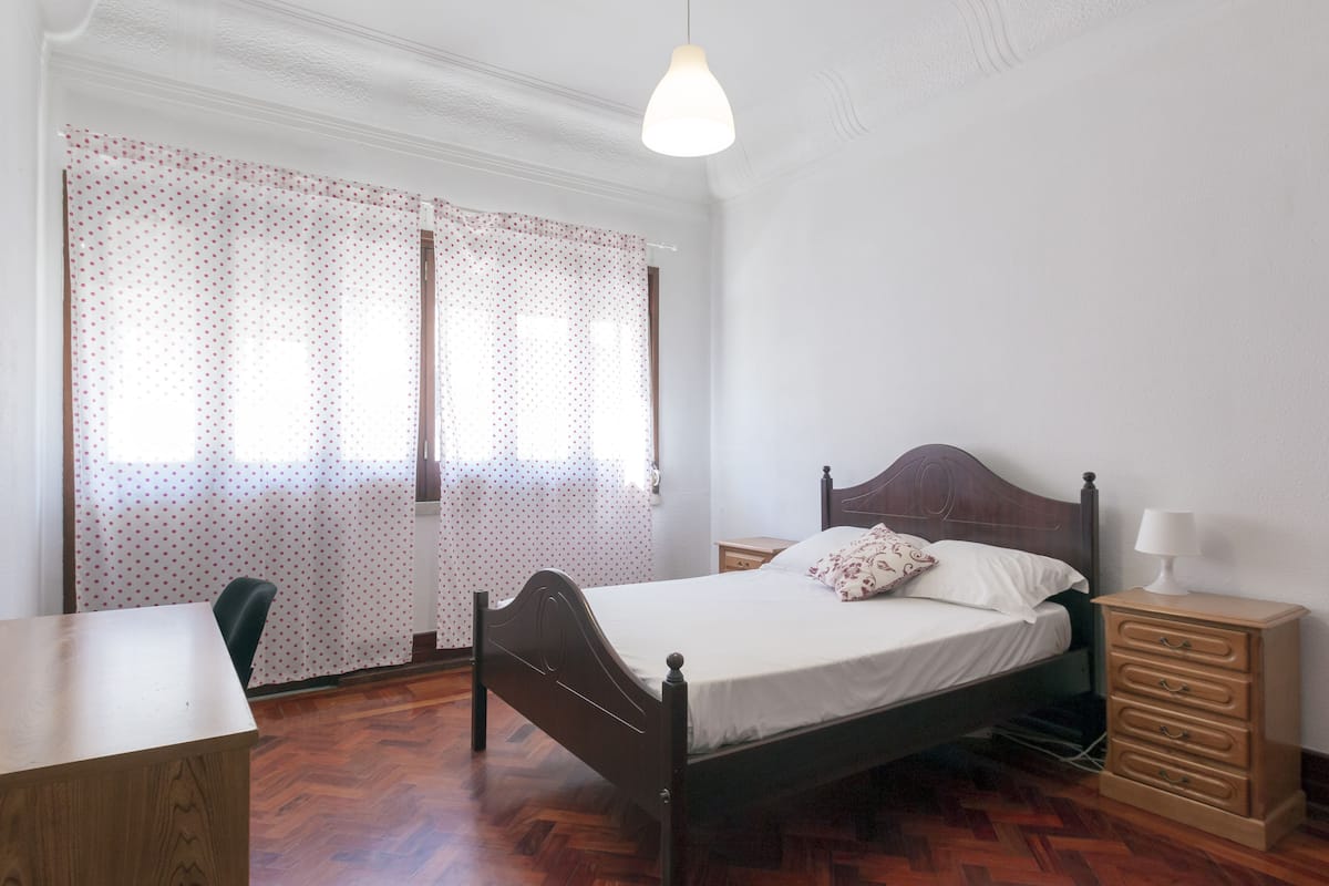 A bedroom with a wooden bed, a nightstand, a desk, and a chair.