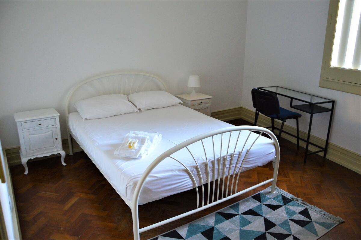 A bedroom with a bed, a nightstand, a desk, and a chair.