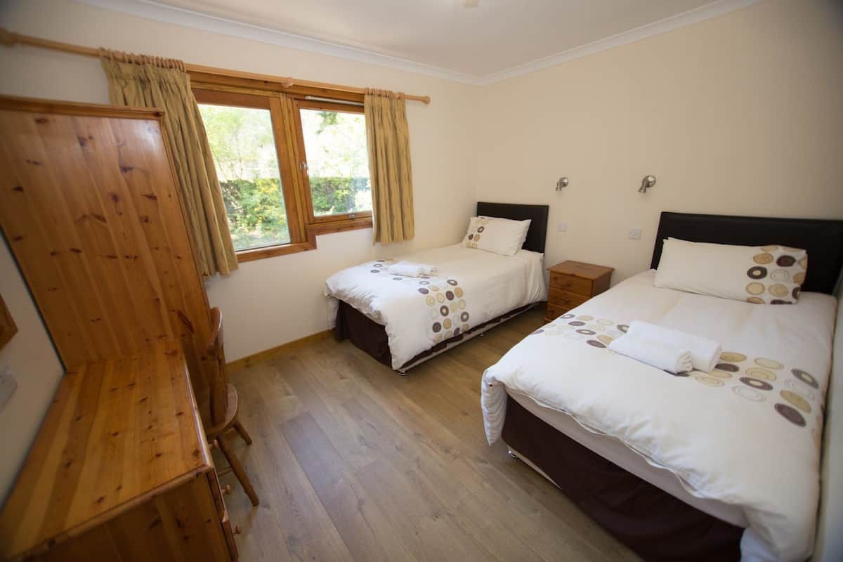 A bedroom with two beds, wooden furniture, and a window with curtains.