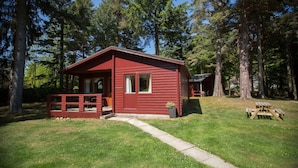 A red cabin with a porch and a picnic table in a forested area. - Invercauld Lodges (Ballater)