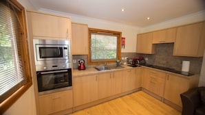 A modern kitchen with wooden cabinets, stainless steel appliances, a window with blinds, and a black countertop. - Invercauld Lodges (Ballater)