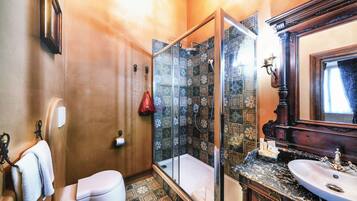 Un baño con cabina de ducha de vidrio, un inodoro blanco, un lavabo con encimera de mármol y un espejo sobre el lavabo.
