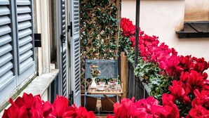 A narrow outdoor corridor with red flowers, a wooden table with a vase, and a lattice wall. - Navona Grand Suite (Rome)
