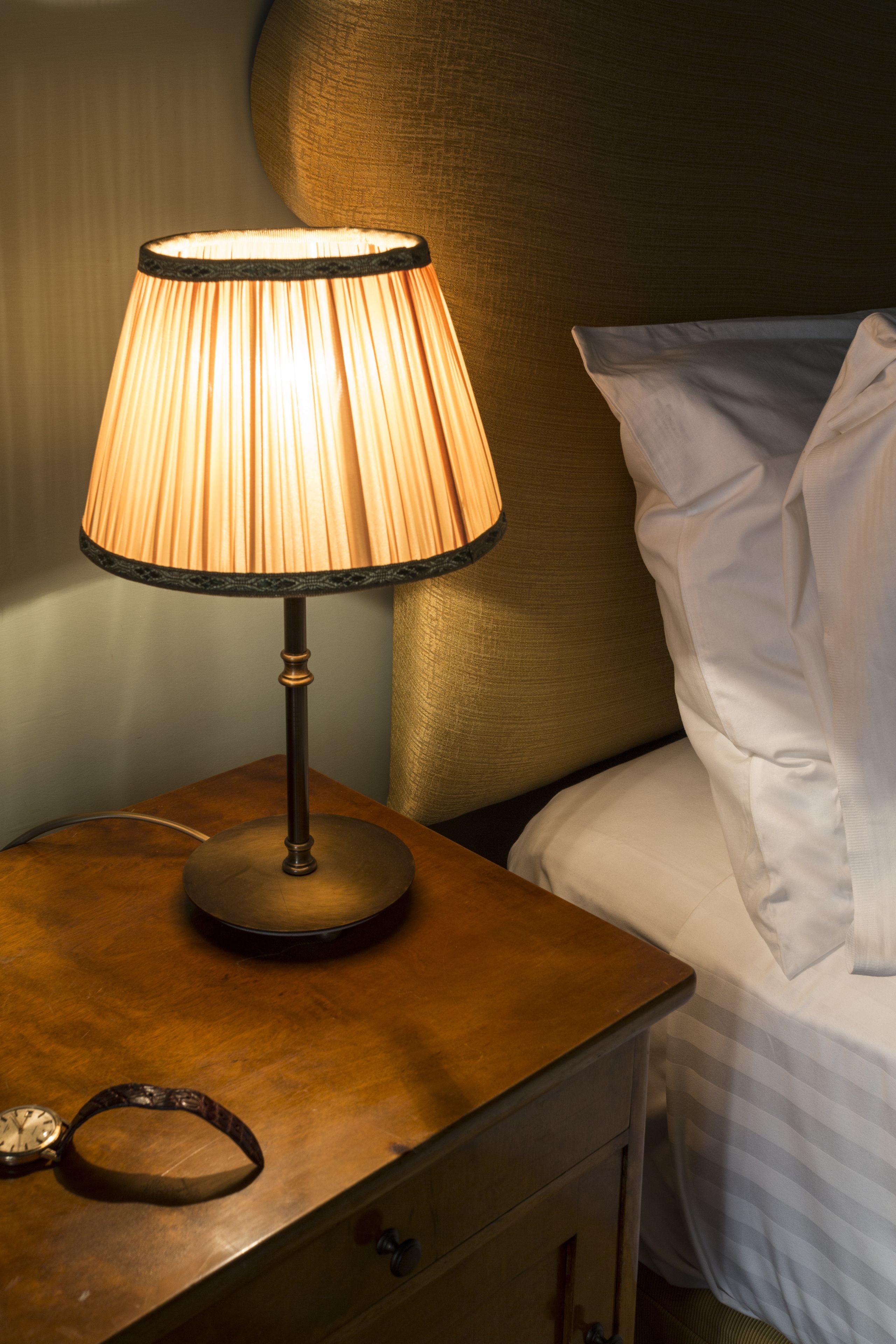 A bedside table with a lamp, a clock, and a drawer.
