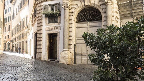 A cobblestone street with a historic building featuring a large arched doorway and a sign reading "BARBIERE". - Navona Grand Suite (Rome)