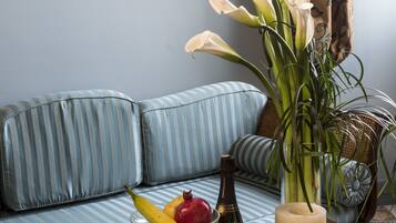 A room with a blue-striped sofa, a tray with glasses and fruits, a vase with white flowers, and a painting on the wall.
