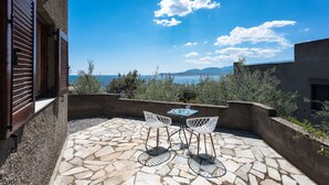 A patio with stone flooring and two white chairs, overlooking a scenic view of the sea and mountains. - Cavo Grosso (East Mani)