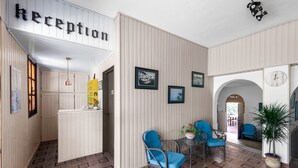 A reception area with a sign, framed pictures, blue chairs, a potted plant, and a clock on the wall. - Cavo Grosso (East Mani)