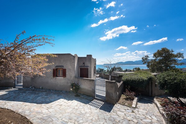 A stone-paved courtyard with a rustic building, a gate, and a view of the sea and mountains. - Cavo Grosso (East Mani)