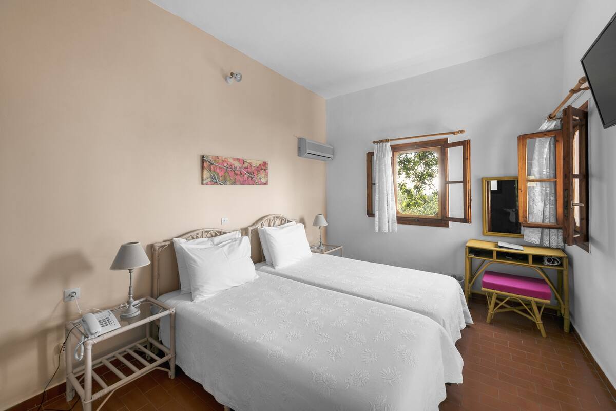 A room with two beds, a desk with a chair, a TV, and an air conditioning unit.