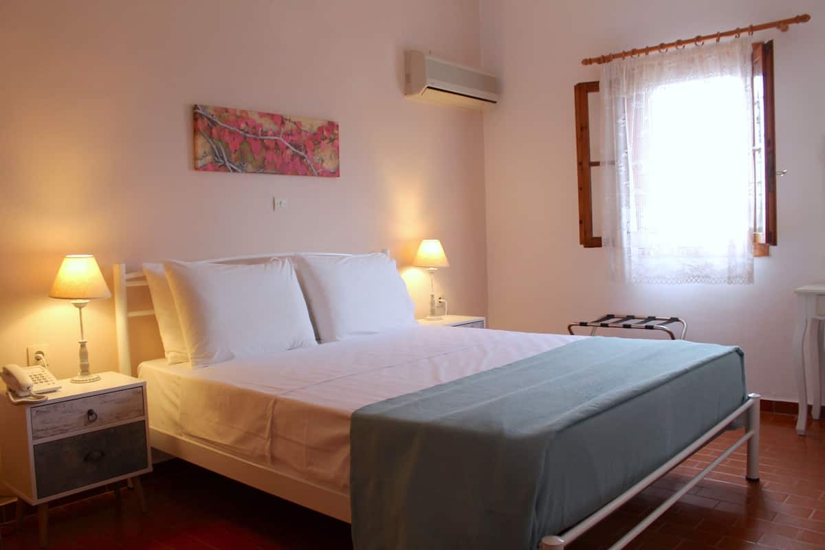 A neatly made bed with white linens, two bedside lamps, a nightstand with a phone, and a painting on the wall.