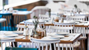 A restaurant with round tables, white chairs, and neatly set dining tables with plates, cutlery, and salt and pepper shakers. - Cavo Grosso (East Mani)