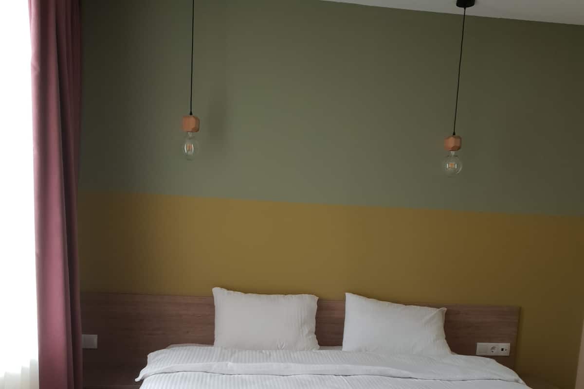 A double bed with a wooden headboard, two bedside tables, and a large window with curtains.