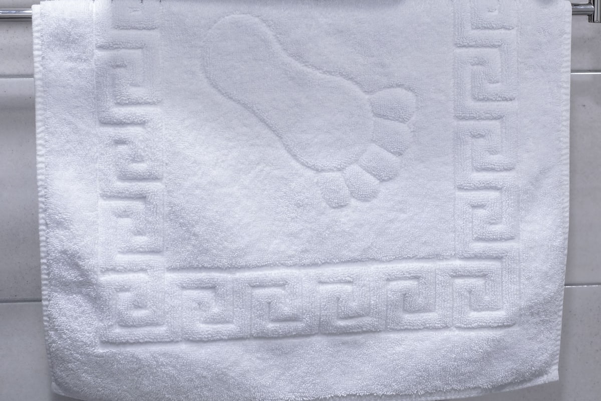 A stack of white towels on a metal towel rack and a single towel with a foot imprint on a bathroom wall.