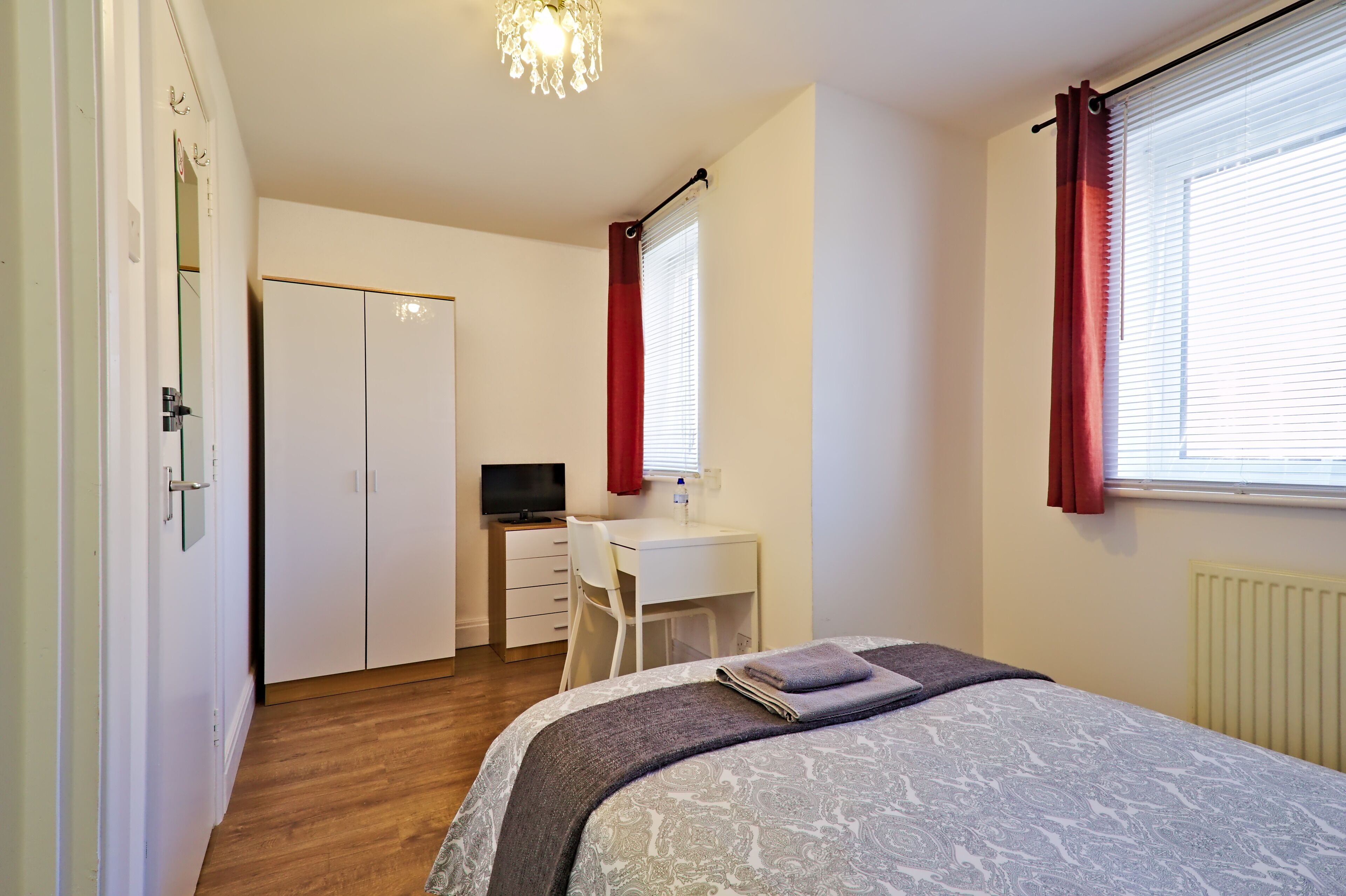 A bedroom with a bed, a desk, a chair, and a television.