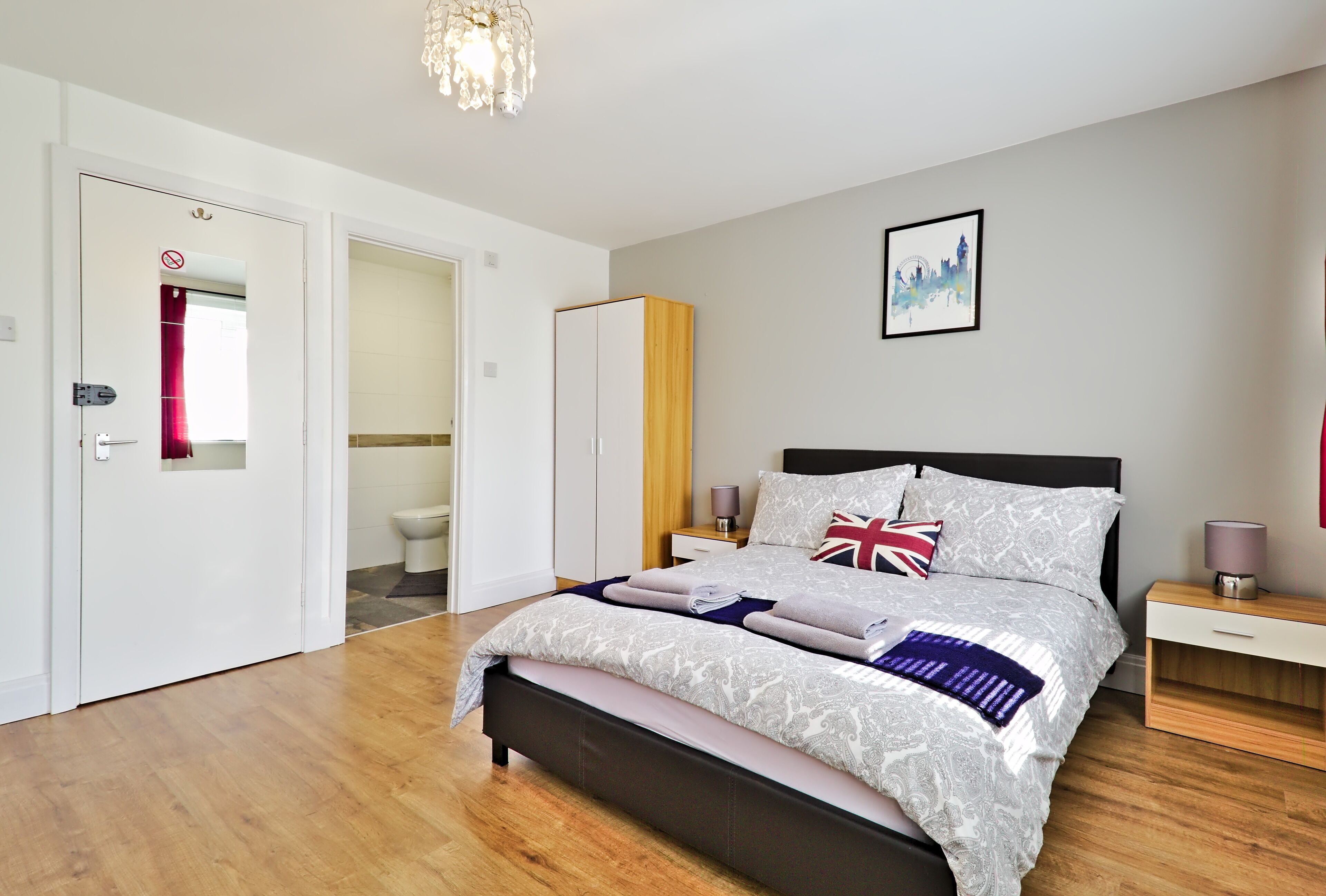 A modern bedroom with a bed, bedside tables, a wardrobe, and a bathroom visible through an open door.