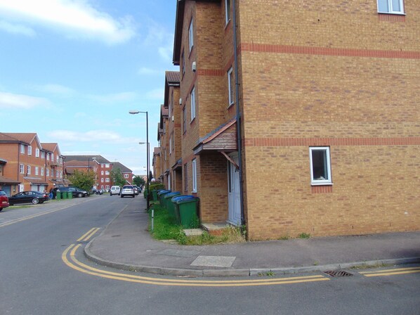 A residential street with brick buildings, parked cars, and green bins along the sidewalk. - Harlinger Lodge (London)