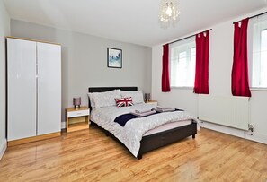 A bedroom with a bed, a wardrobe, a bedside table, a lamp, and a window with curtains. - Harlinger Lodge (London)