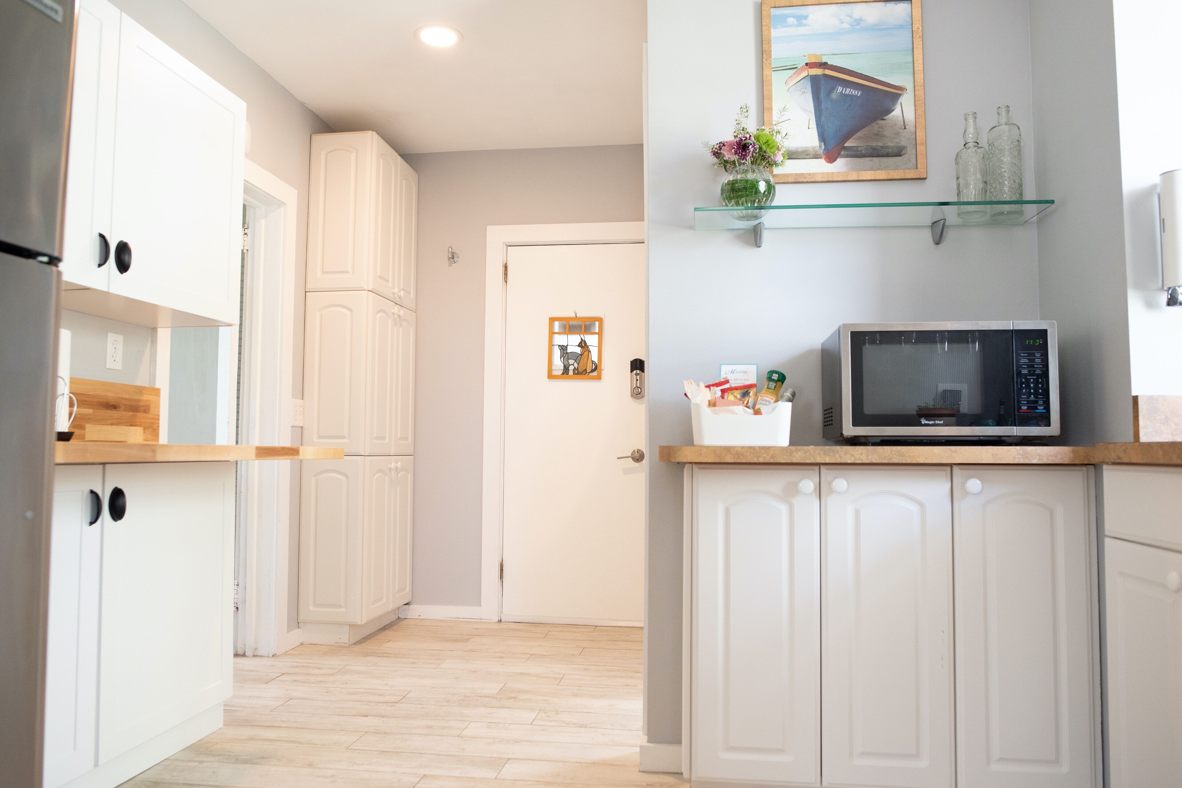 Una cocina moderna con armarios blancos, un microondas y una repisa de vidrio con objetos decorativos.