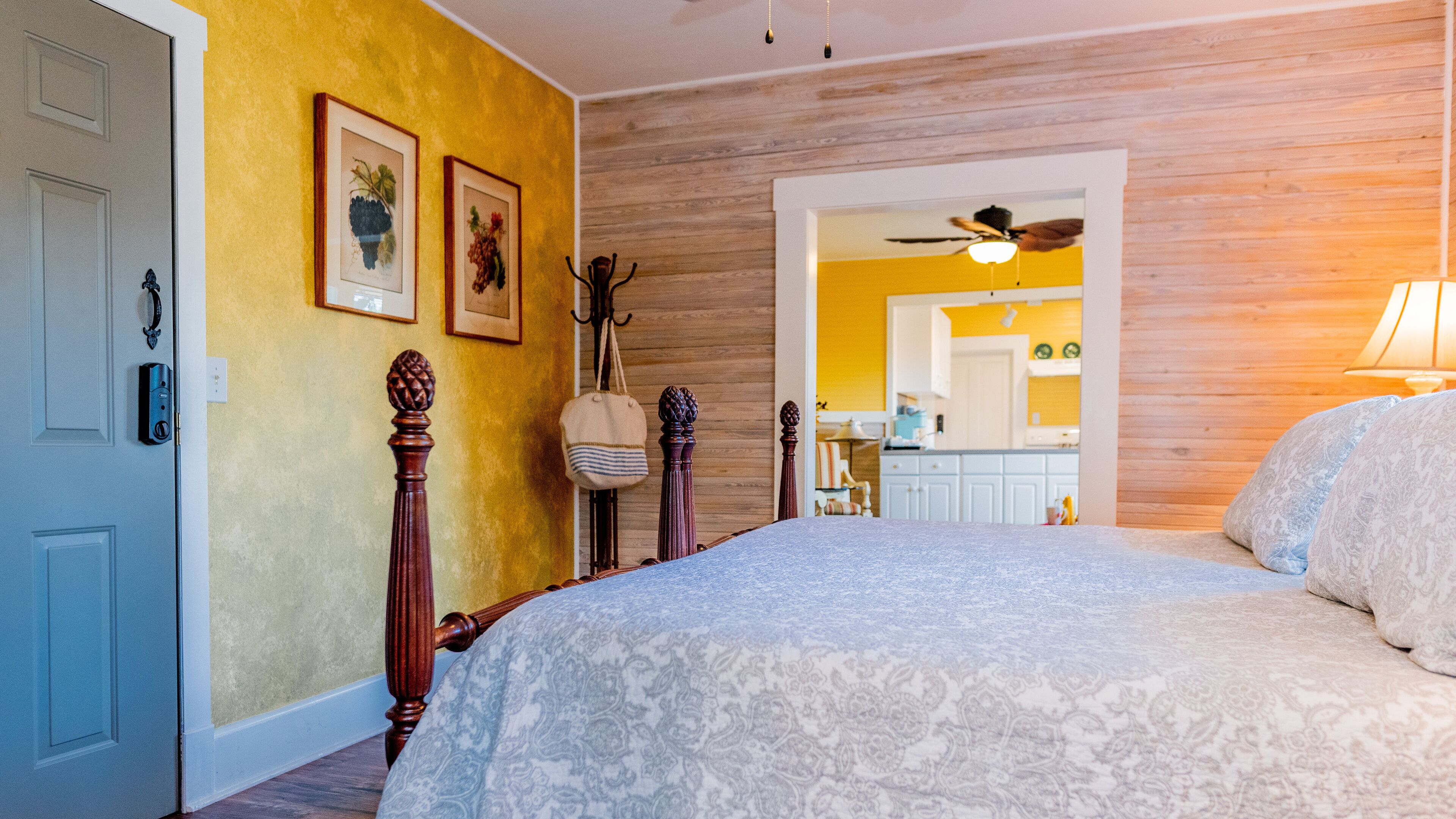 A bedroom with a bed, wooden headboard, and a view into the kitchen.