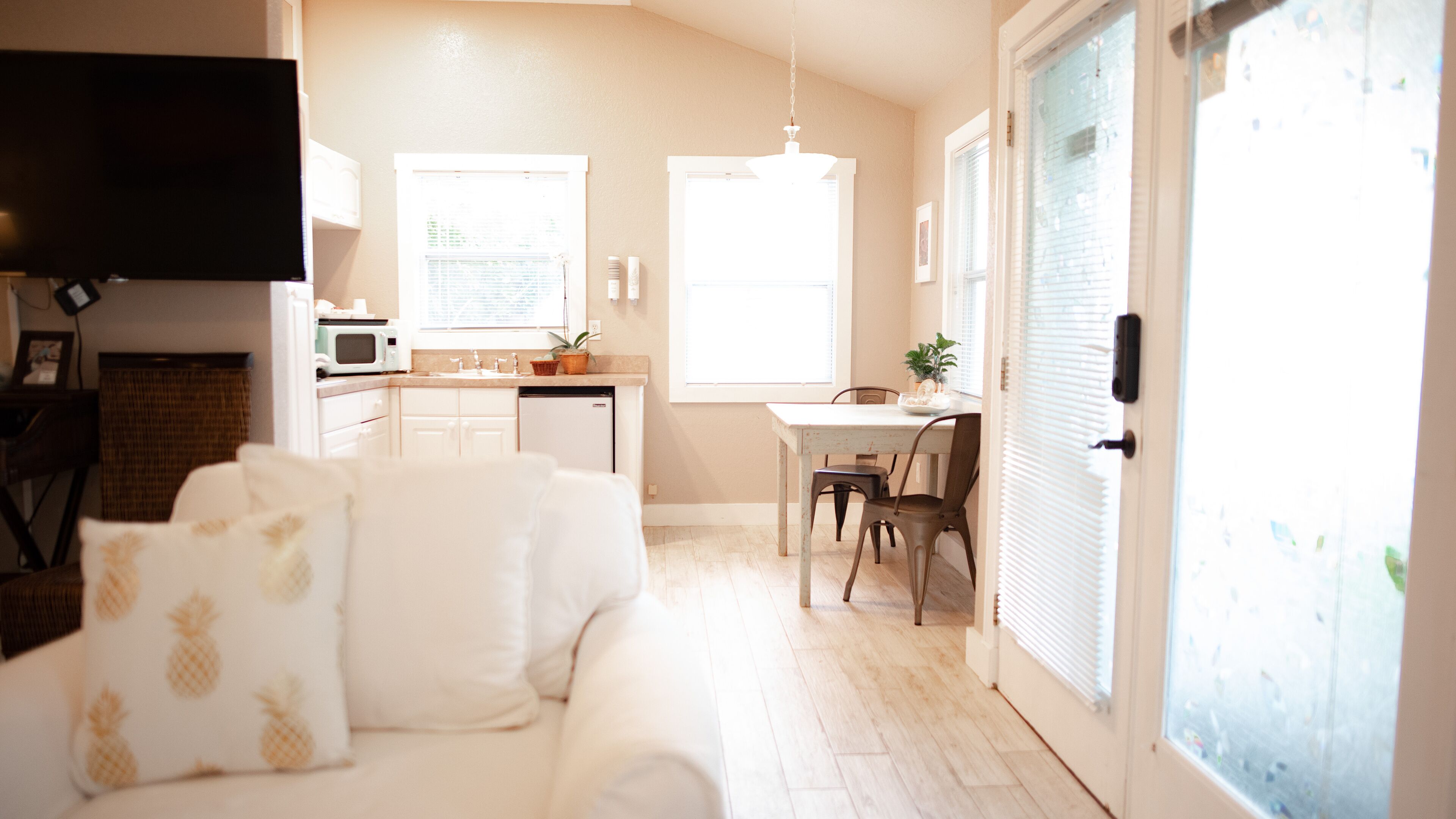 Una sala de estar luminosa con un sofá blanco, una zona de cocina con microondas y una mesa de comedor con sillas.