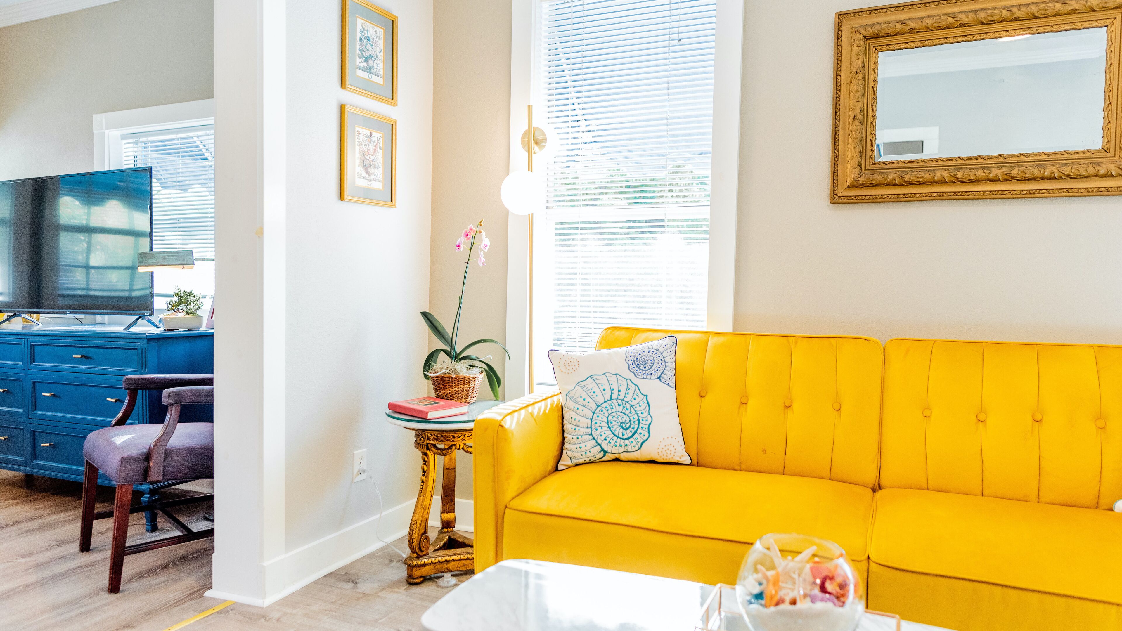 A living room with a yellow sofa, a blue dresser, a television, and a small table with a plant.