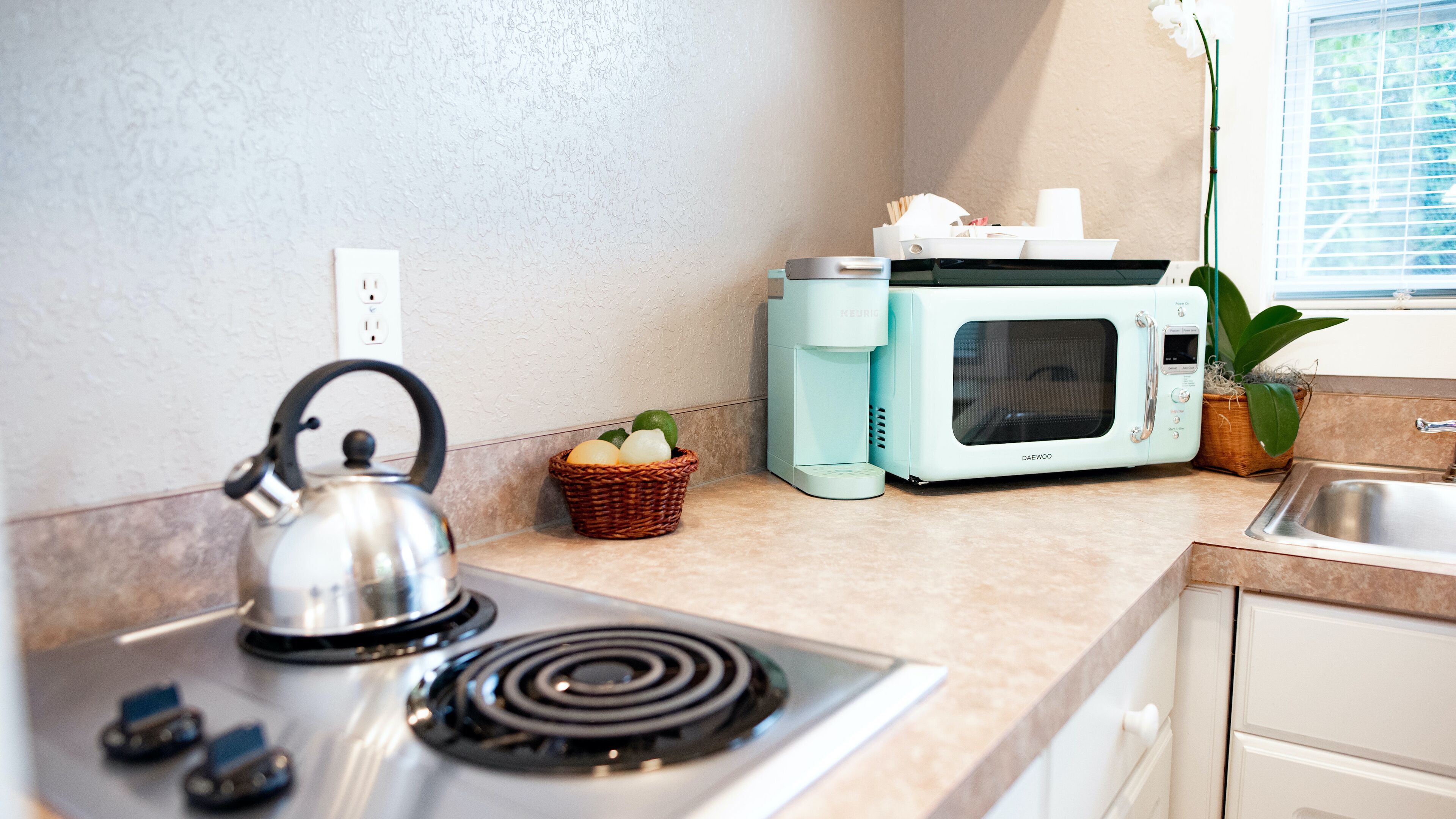 A kitchen with a kettle, a microwave, a basket of fruit, and a sink.