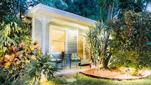 A small, single-story house with a porch, surrounded by lush greenery and a variety of plants. - Meranova Guest Inn (Dunedin)
