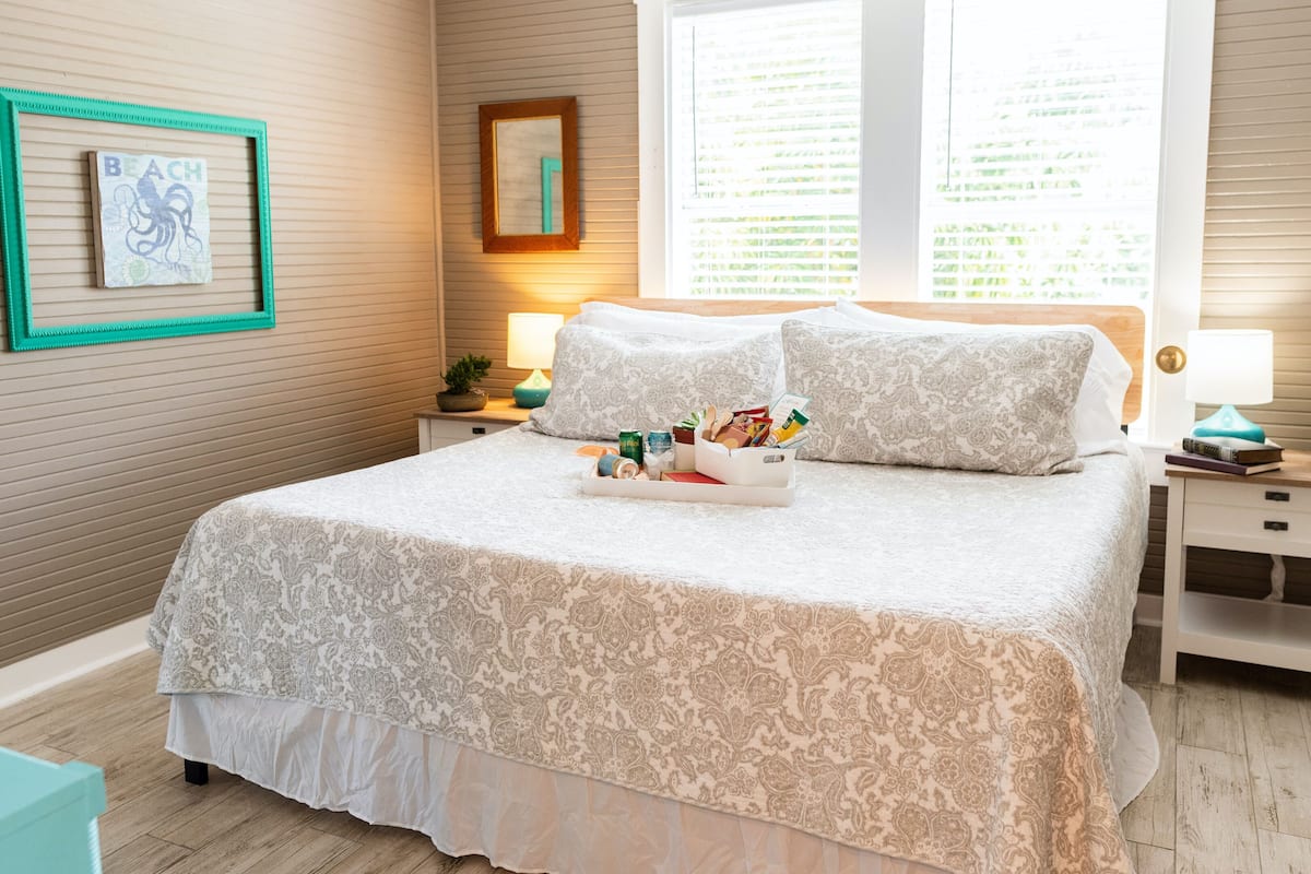 A neatly made bed with a tray of breakfast items, a bedside table with a lamp, and a framed picture on the wall.