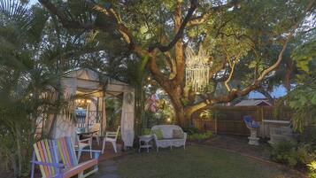 Un espace patio aménagé avec du mobilier d’extérieur, une pergola et un grand arbre qui offre de l’ombre.