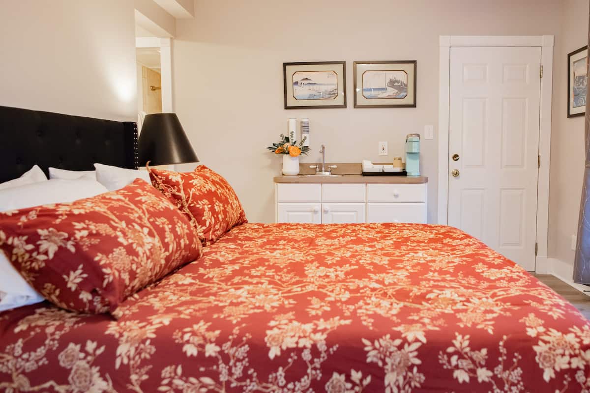 A bedroom with a large bed, a nightstand, a dresser, and a window with curtains.