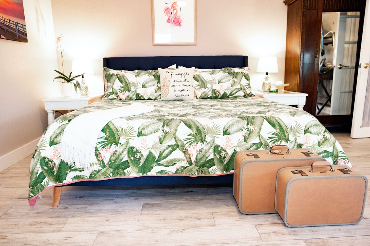 A bedroom with a bed, two bedside tables, a nightstand, a wall-mounted picture, and two suitcases.