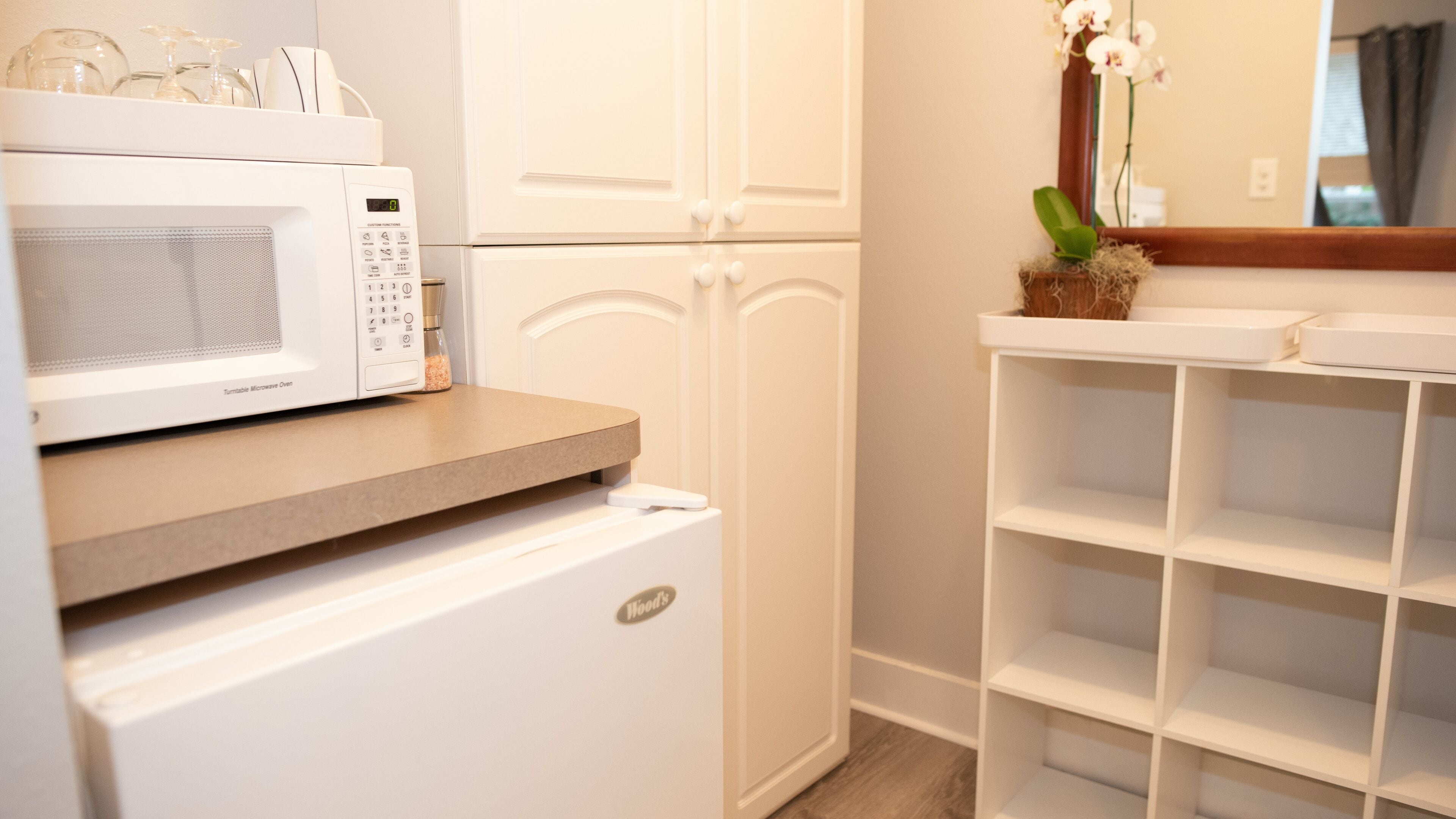 A kitchen with a microwave, a small refrigerator, and a white cabinet.