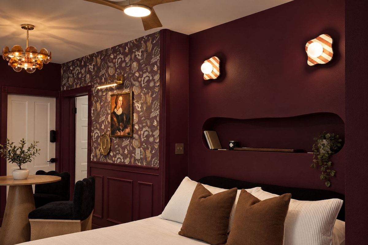 A bedroom with a bed, a desk, a chair, a ceiling fan, and wall-mounted lights.